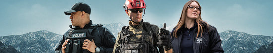 Three emergency responders—a police officer, a firefighter, and an EMT—stand in uniform outdoors with mountains in the background.