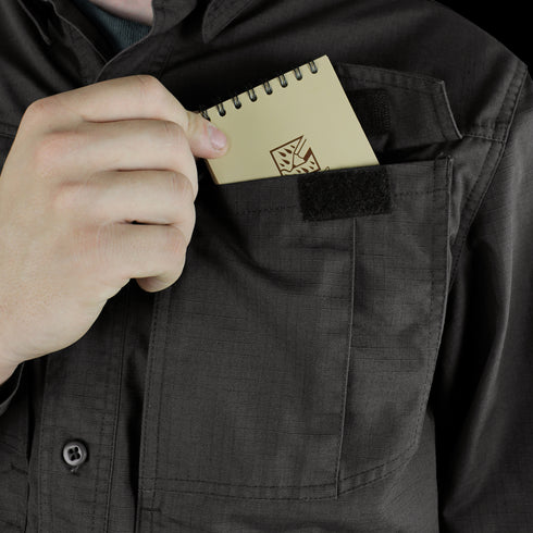 A person slips a compact, spiral-bound notebook into the chest pocket of a Condor Tac-Pro Shirt, ready for quick notes—just like a first responder prepping for duty.