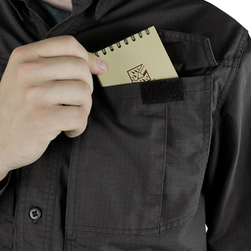 Someone wearing a Condor Tac-Pro Shirt places a small spiral notepad with a geometric design into the Velcro-closed chest pocket.