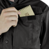 Someone wearing a Condor Tac-Pro Shirt places a small spiral notepad with a geometric design into the Velcro-closed chest pocket.