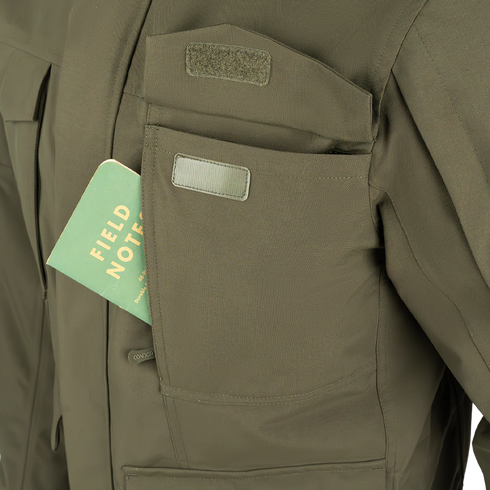 A green Field Notes notebook partially tucked into the chest pocket of a Condor Aegis Waterproof Parka.