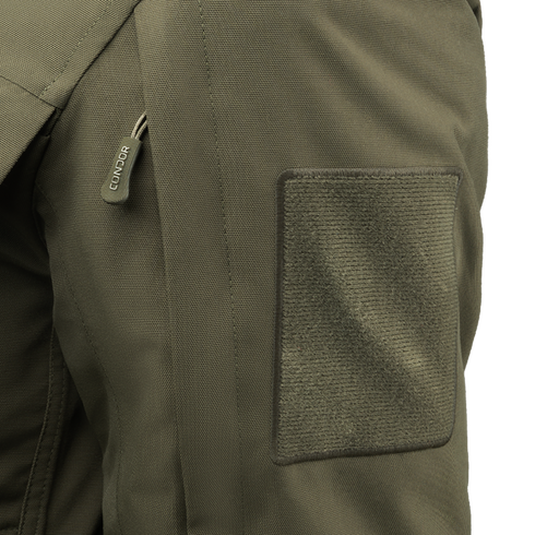 Close-up of an olive green Aegis Waterproof Parka pocket featuring a zipper pull labeled Condor and a large rectangular Velcro patch.