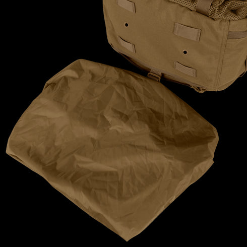 A folded brown tarp is placed next to a Condor Orion Assault Backpack 50L, a tan bushcraft or EDC pack with straps and loops, resting on a light surface.