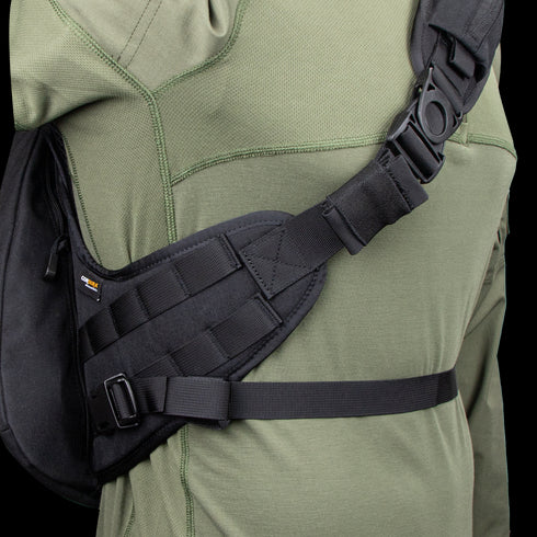 A close-up of a person wearing the Condor Elite Sector Sling Bag 18L by Condor, featuring black tactical straps with clips and padding, over an olive green long-sleeve shirt.
