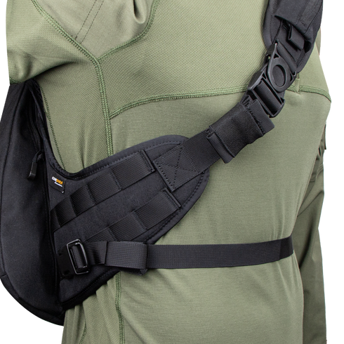 A close-up of a person wearing the Condor Elite Sector Sling Bag 18L by Condor, featuring black tactical straps with clips and padding, over an olive green long-sleeve shirt.