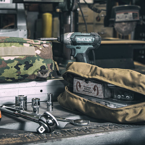 A tactical Condor Kit Bag - MultiCam Black with a Makita power tool, socket wrenches, a camouflage pouch, and a Blood Stopper First Aid Dressing—ideal for first responders or law enforcement.