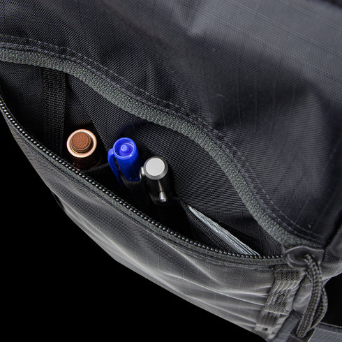 Close-up of the open zippered pocket on the Condor Aero Roll-Top Backpack 25L, holding a brown pen, blue pen, black pen, and metallic gray pen—gear favored by military and first responders.
