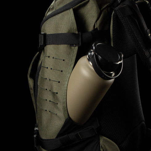 A khaki water bottle sits in the side pocket of a Condor Nomad Backpack 25L in olive green, featuring black straps and webbing.
