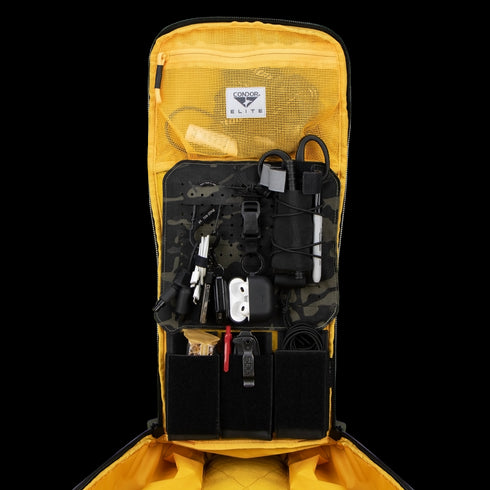 The Condor Nomad Backpack 25L in yellow showcases organized compartments holding EDC essentials—electronics, cables, multitool, flashlight, and gear—for first responders or range trips.