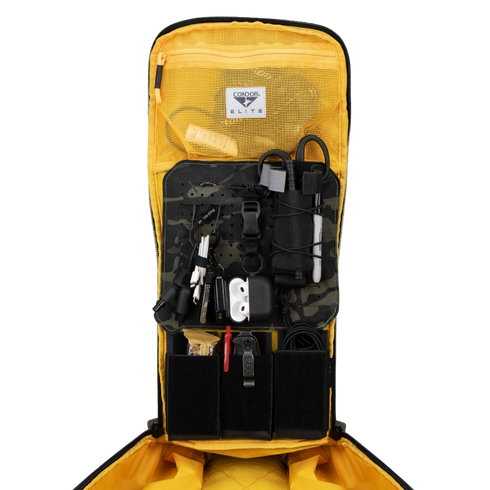 The Condor Nomad Backpack 25L is open, showing gadgets, cables, pens, a flashlight, and tools neatly arranged in mesh and elastic compartments.