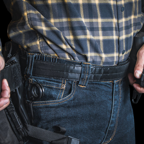 A person wearing a plaid shirt and jeans with a Condor Inner Belt, carrying a holstered handgun on their waistband, resembles an off-duty law enforcement officer.