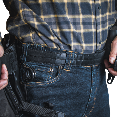 A person wearing a plaid shirt and jeans with a Condor Inner Belt, carrying a holstered handgun on their waistband, resembles an off-duty law enforcement officer.