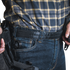 A person wearing a plaid shirt and jeans with a Condor Inner Belt, carrying a holstered handgun on their waistband, resembles an off-duty law enforcement officer.