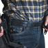 A person wearing a plaid shirt and jeans with a Condor Inner Belt, carrying a holstered handgun on their waistband, resembles an off-duty law enforcement officer.