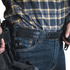 A person wearing a plaid shirt and jeans with a Condor Inner Belt, carrying a holstered handgun on their waistband, resembles an off-duty law enforcement officer.