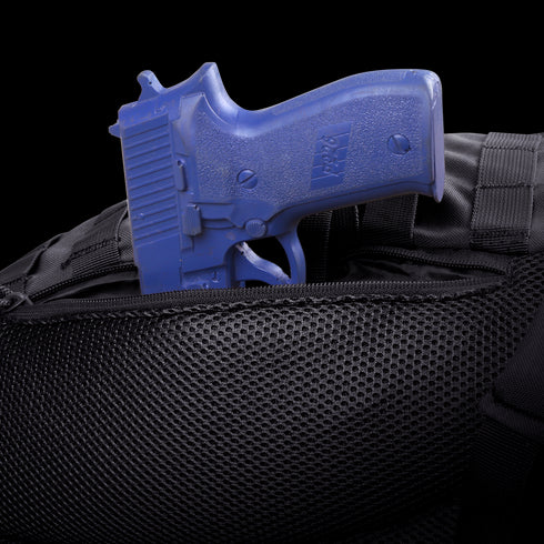 A blue training handgun is partially tucked into the zippered pocket of the Condor Ambidextrous Sling 27L, a black tactical bag made with mesh material.