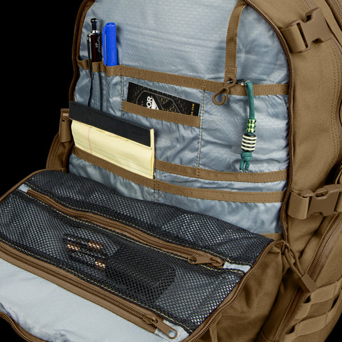 The Condor Commuter Backpack 26L opens to reveal an organized interior with pens, notepad, cards, cord, and mesh zippered pockets for small items—perfect for bushcraft enthusiasts who value efficiency and preparedness.