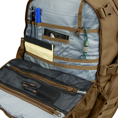 The Condor Commuter Backpack 26L is shown open against a light background, displaying an organized interior with pens, a notepad, knife, paracord, and mesh zippered pockets holding various small items.