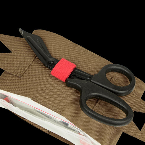 A pair of black trauma shears with a red band, favored by first responders, rests on a Condor Micro TK Pouch Gen II with a partially open zippered compartment.