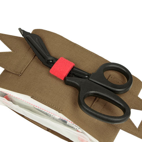 A pair of black trauma shears with a red band, favored by first responders, rests on a Condor Micro TK Pouch Gen II with a partially open zippered compartment.