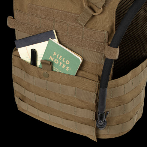 A tan Condor Gunner Plate Carrier holds a black pen, a black notebook, and a green Field Notes notebook—everyday essentials for first responders—with a hydration tube attached.