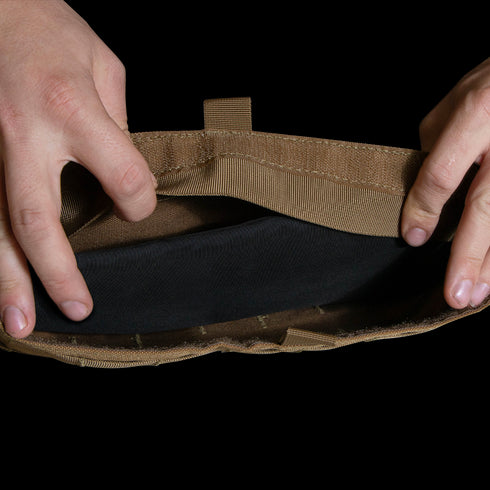 Two hands open a tan Enforcer Releasable Plate Carrier by Condor, revealing black interior details and MOLLE webbing against a white background.