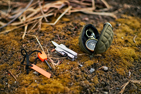 The Condor Grenade Key Chain Pouch holds a multitool, fire starter, and compass with tactical style, set on mossy ground with dry grass in the background.