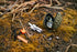 The Condor Grenade Key Chain Pouch holds a multitool, fire starter, and compass with tactical style, set on mossy ground with dry grass in the background.