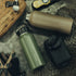 Two Condor Vacuum Sealed Thermal Bottles—one green, one brown—rest beside a tactical pouch, gloves, black case, fishing net, multitool, and yellow walkie-talkie: a perfect EDC lineup for bushcraft enthusiasts.