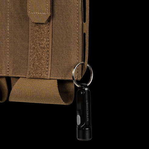 A small black flashlight on a keyring is attached to the brown fabric loop on the side of the Condor VAS Flex Placard tactical pouch.