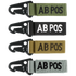 The Condor Blood Type Key Chain set includes four keychains embroidered with “AB POS” in green, black, tan, and grey, each featuring a black metal clip.