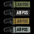 The Condor Blood Type Key Chain set includes four keychains embroidered with “AB POS” in green, black, tan, and grey, each featuring a black metal clip.