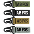 The Condor Blood Type Key Chain set includes four keychains embroidered with “AB POS” in green, black, tan, and grey, each featuring a black metal clip.