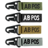 The Condor Blood Type Key Chain set includes four keychains embroidered with “AB POS” in green, black, tan, and grey, each featuring a black metal clip.