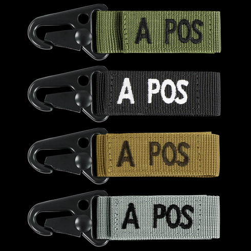 The Condor Blood Type Key Chain set includes four keychains with black metal clips and fabric straps in green, black, brown, and gray, each featuring “A POS” embroidered text.