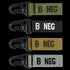 The Condor Blood Type Key Chain set includes four keychains with plastic clips and fabric straps in green, black, tan, and gray, each boldly labeled with B NEG to display your blood type.