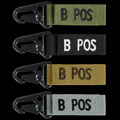 The Condor Blood Type Key Chain set features four keychains with plastic clips and fabric tags labeled B POS, available in green, black, tan, and gray.
