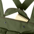 A small spiral notebook partially tucked into the front pocket of a Condor 7-Pocket Chest Rig in olive green, featuring metal snap buttons.