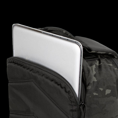 A silver laptop is partially tucked into the front compartment of the Condor Prime Pack 21L - MultiCam Black backpack.
