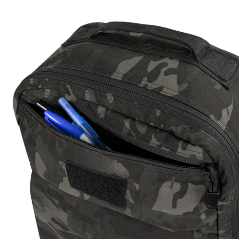 A close-up of the Condor Prime Pack 21L in MultiCam Black with its front zipper pocket open, revealing two blue pens and one black pen inside.