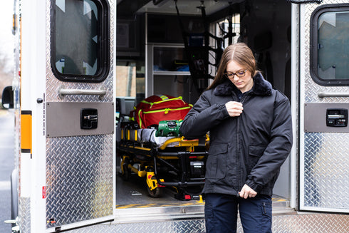 A person in tactical uniform zips up the Condor Guardian Duty Jacket | SALE while standing at the open ambulance doors, with medical equipment visible inside.