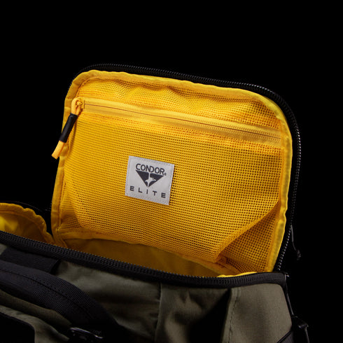 The Condor Nomad Backpack 25L in olive green has a yellow mesh zippered pocket inside the lid with a Condor label—ideal for EDC or first responders.