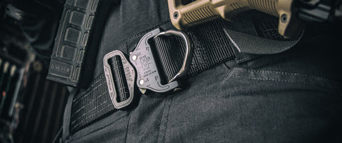 Close-up of the Condor Cobra Pro Belt, featuring a metal quick-release buckle, worn over dark pants and equipped with tactical gear in a rugged outdoor setting.