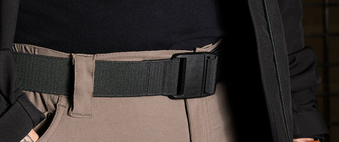 Close-up of a person wearing khaki pants and a Condor PDQ Magnetic Belt | SALE with a plastic buckle, paired with a black shirt and partially covered by a black jacket.