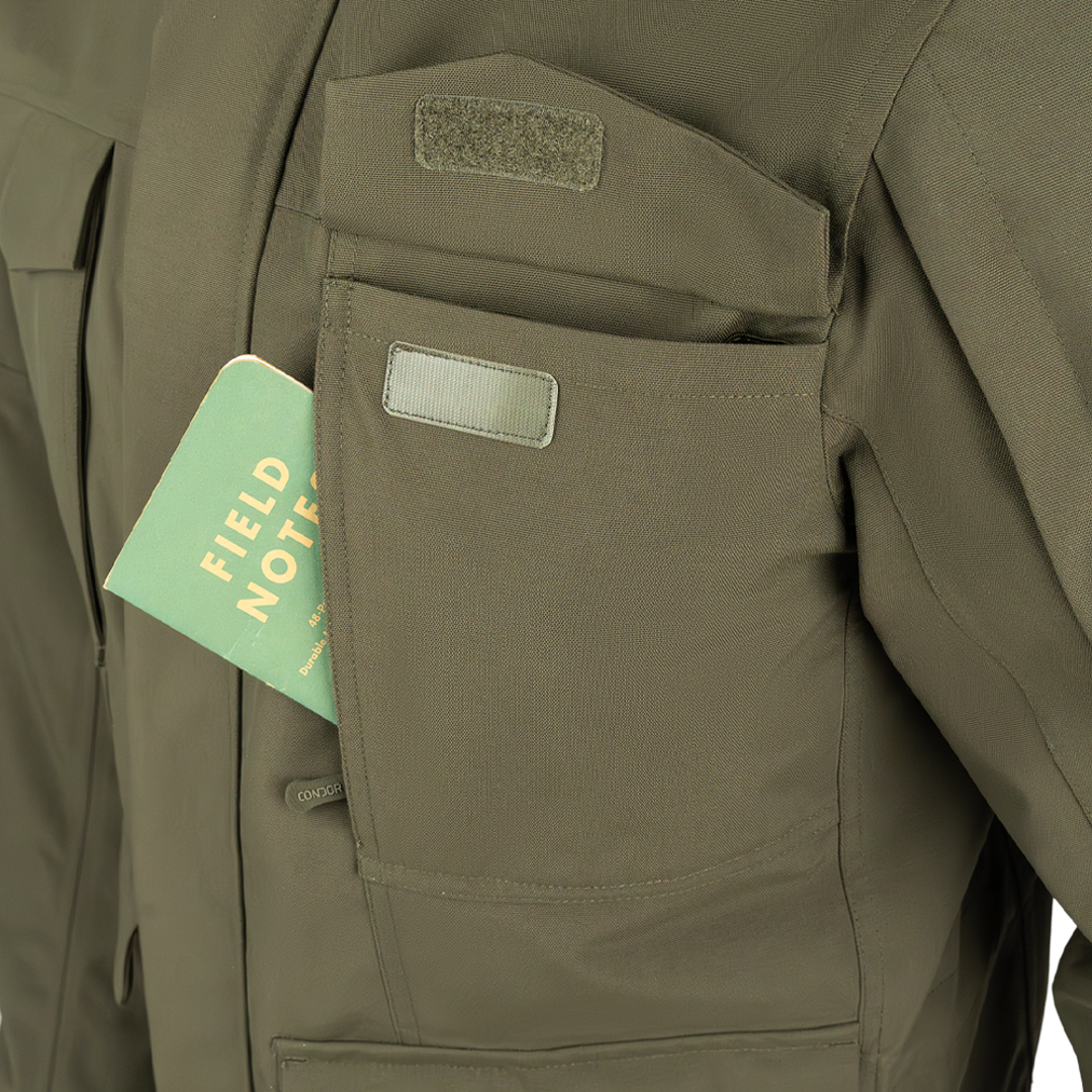 A green Field Notes notebook partially tucked into the chest pocket of a Condor Aegis Waterproof Parka.