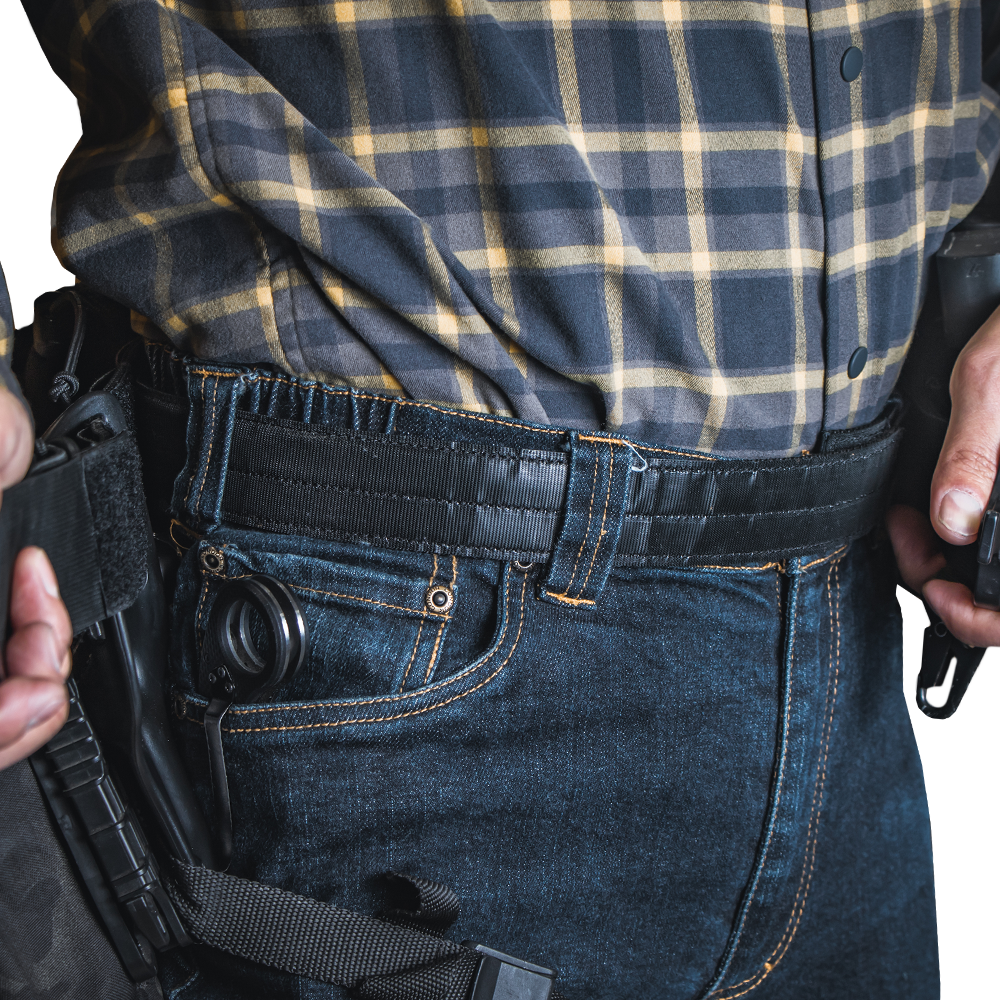 A person wearing a plaid shirt and jeans with a Condor Inner Belt, carrying a holstered handgun on their waistband, resembles an off-duty law enforcement officer.