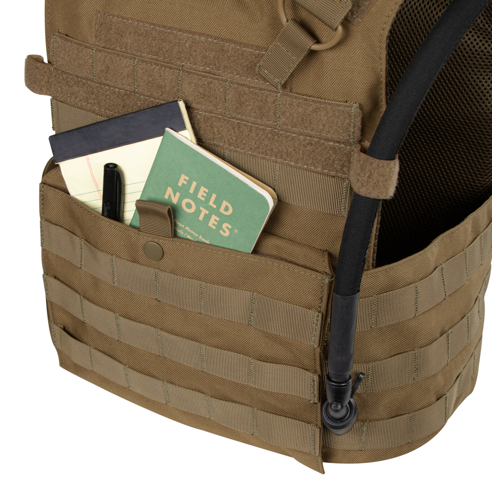 A tan Condor Gunner Plate Carrier holds a black pen, a black notebook, and a green Field Notes notebook—everyday essentials for first responders—with a hydration tube attached.