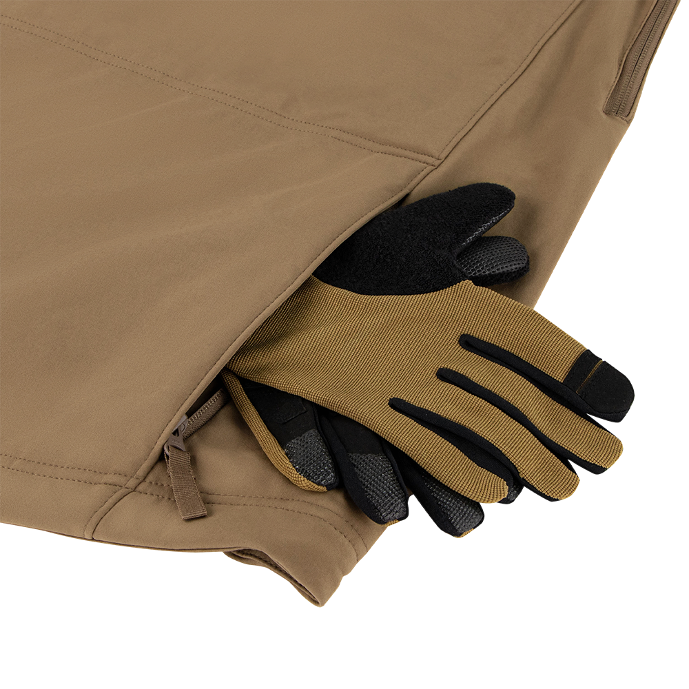 A Summit Zero Softshell Jacket by Condor in tan has tan and black work gloves partially tucked into its zippered side pocket.
