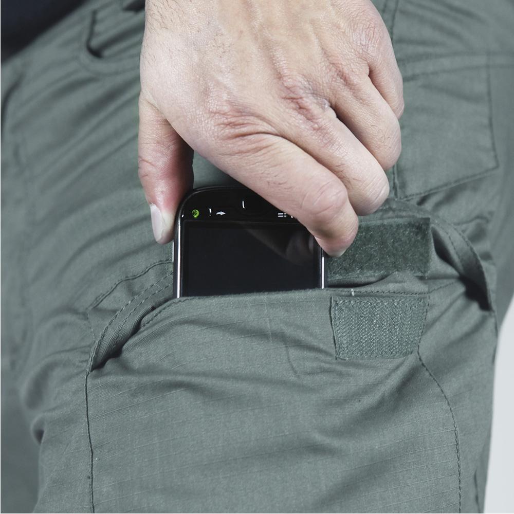 A persons hand slips a smartphone into the small cargo pocket of Condor Stealth Operator Pants.