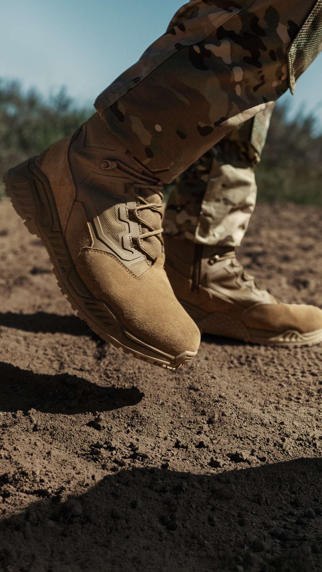 A person wearing camouflage pants and Condor Brigade 8″ Tactical Boots - AR670 walks on dry, sandy ground outdoors.